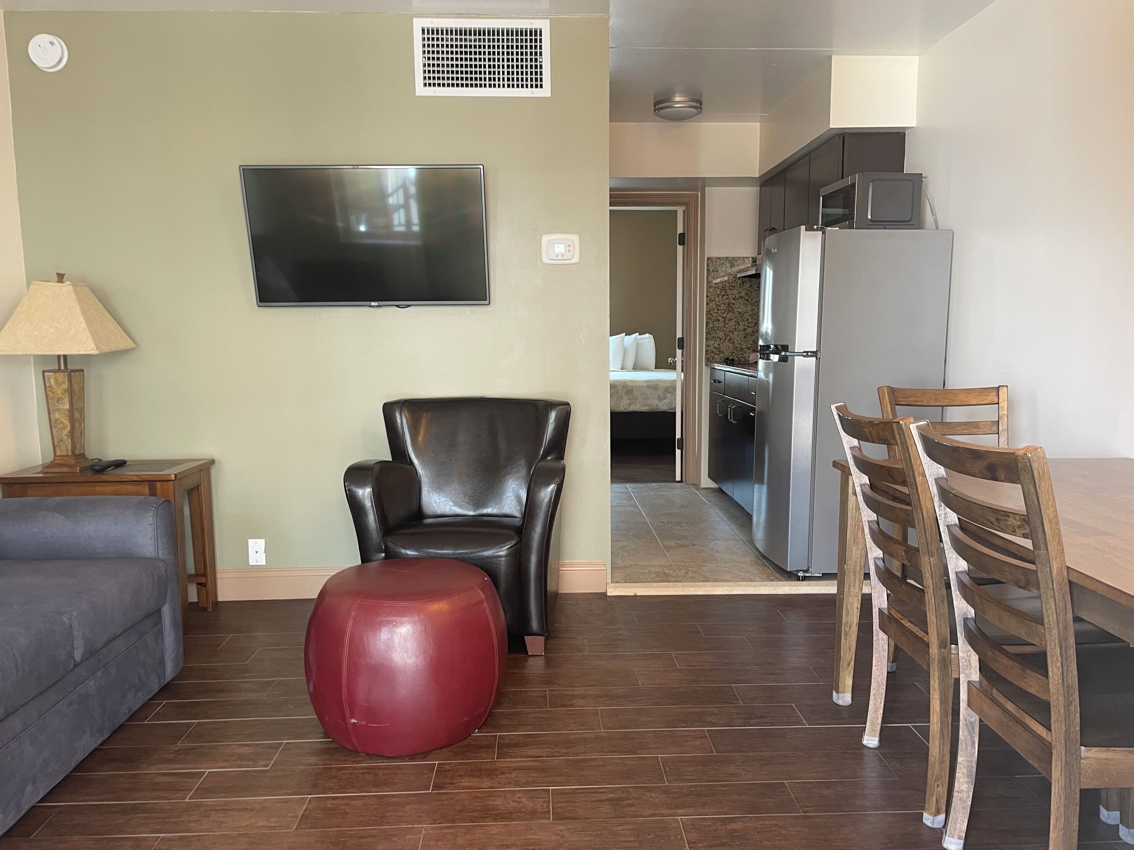 A living room with a sofa, a red ottoman, a leather chair, and a TV mounted on the wall.