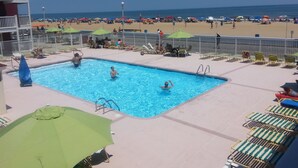 A swimming pool with lounge chairs and umbrellas, a beach in the background, and a clear sky. - Fish Tales Boardwalk Inn (Ocean City)