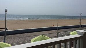 A beach view from a balcony with a wooden deck and green umbrellas. - Fish Tales Boardwalk Inn (Ocean City)