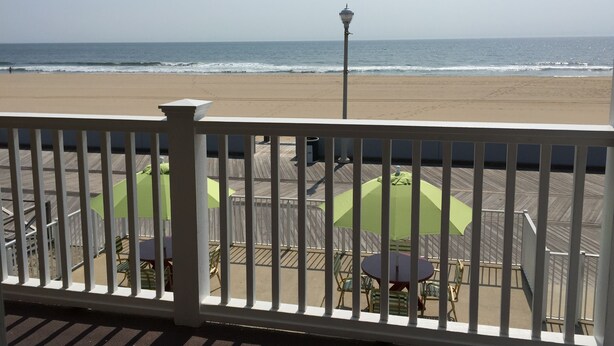 A wooden deck with outdoor seating and a view of the beach. - Fish Tales Boardwalk Inn (Ocean City)