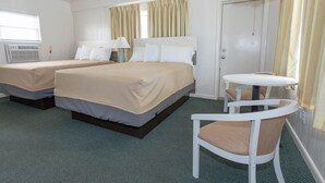 A hotel room with two beds, a small table with a chair, a lamp, and a door. - Fish Tales Boardwalk Inn (Ocean City)