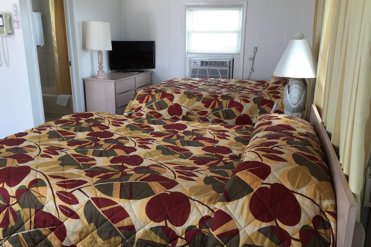 A hotel room with a bed, a TV, an air conditioning unit, and a bathroom visible through an open door.