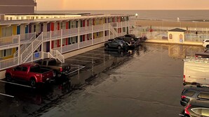 A multi-story motel with colorful exterior walls, a parking lot, and a view of the ocean. - Fish Tales Boardwalk Inn (Ocean City)