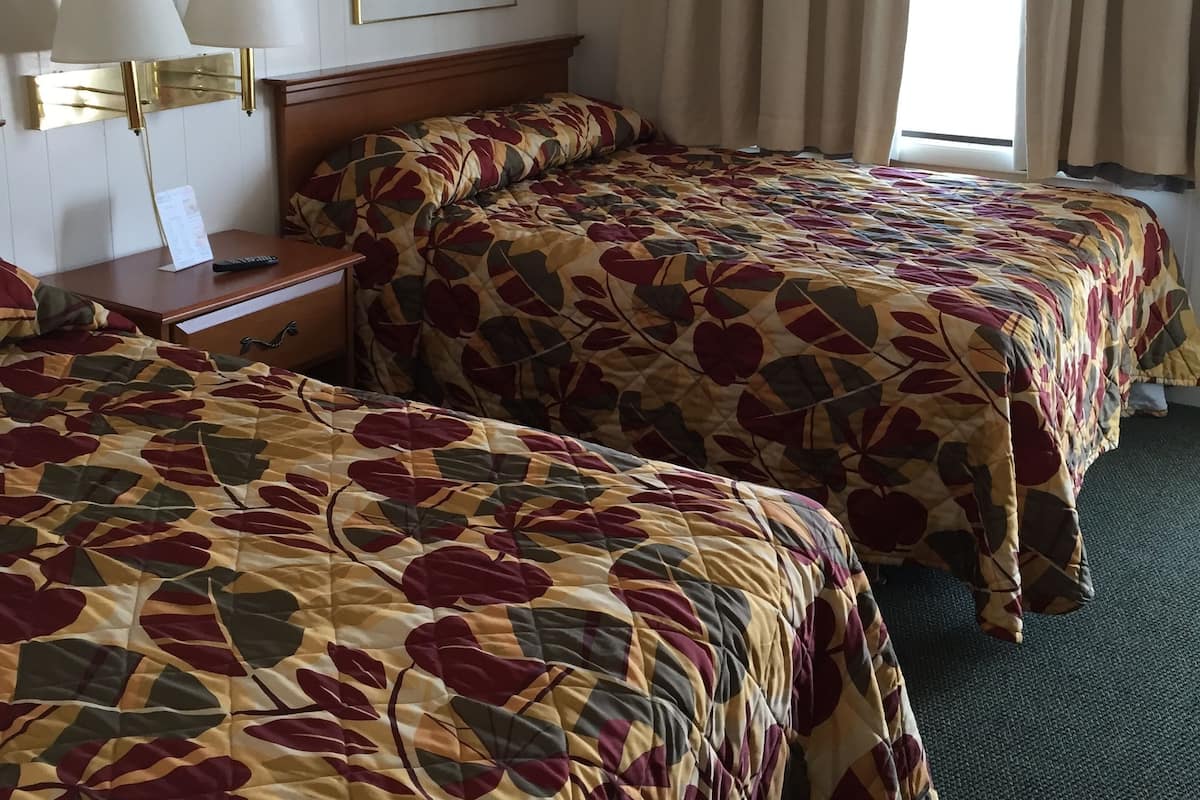 A hotel room with two beds, a nightstand, a lamp, a framed picture, and a window with curtains.