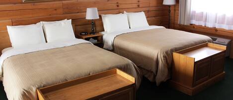 A room with two beds, wooden headboards, and a nightstand with a lamp.