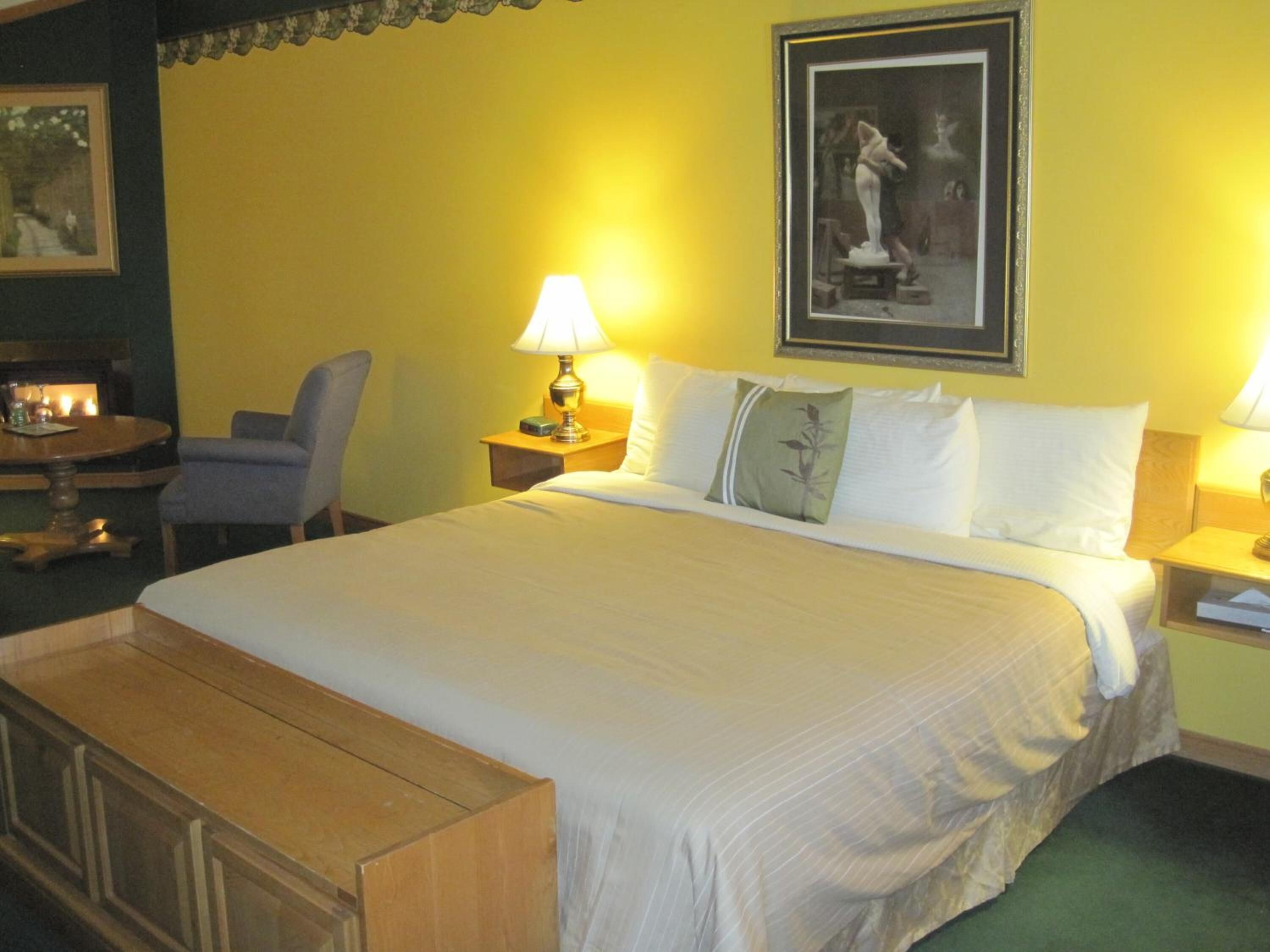 A hotel room with a large bed, two bedside tables with lamps, a chair, a small table with a lamp, and a framed picture on the wall.