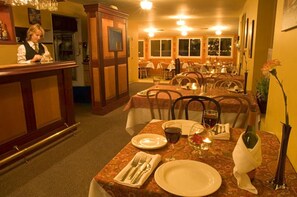 A restaurant interior with a bar area, dining tables, chairs, and a waitress.