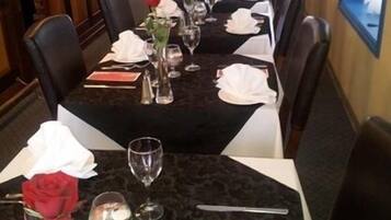 Una larga mesa de comedor con manteles blancos, sillas negras y cubertería dispuesta con cuidado.