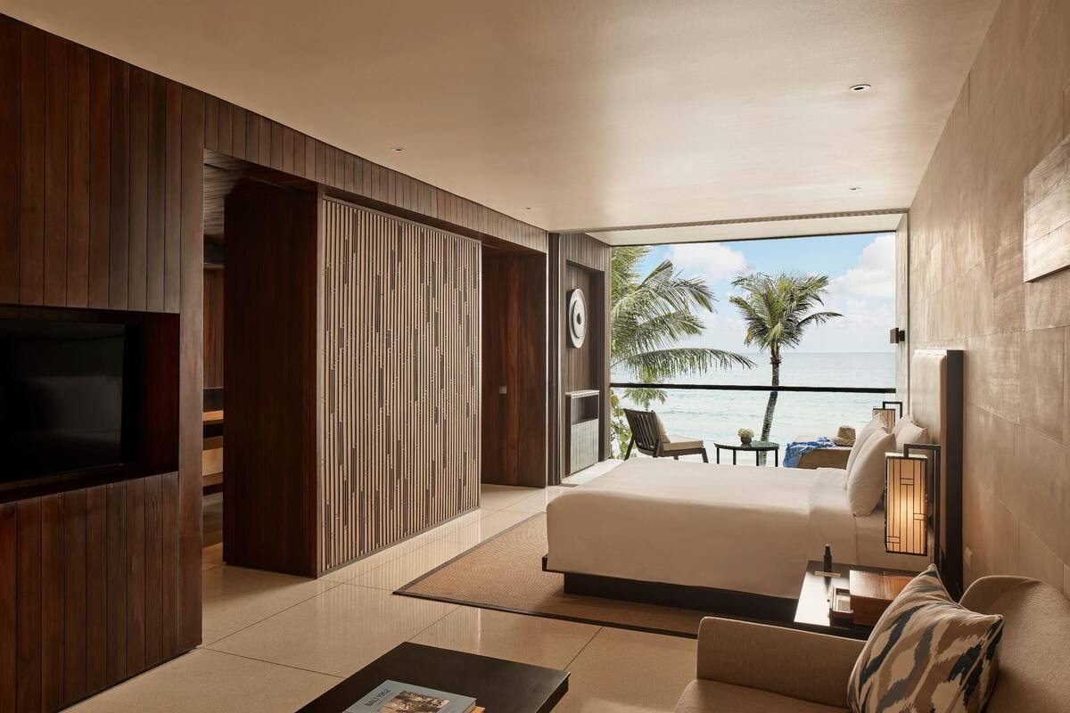 Una camera d'albergo moderna con un letto grande, una TV, un tavolino con dei libri e un balcone con vista sull'oceano.