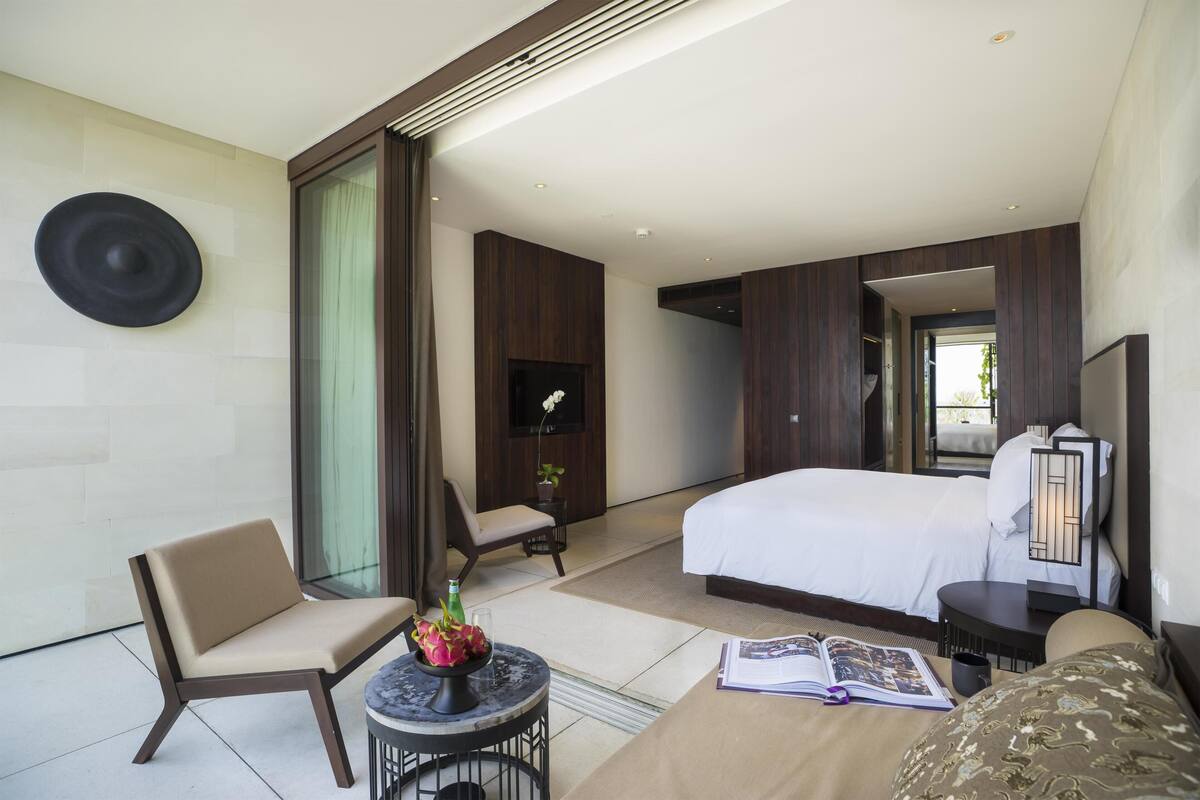 Una moderna camera d'albergo con un letto grande, un'area salotto con una poltrona e un tavolino, una TV a schermo piatto e un'ampia finestra.