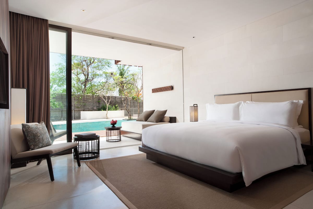 A modern bedroom with a large bed, a sofa, a small table, and a view of a swimming pool.