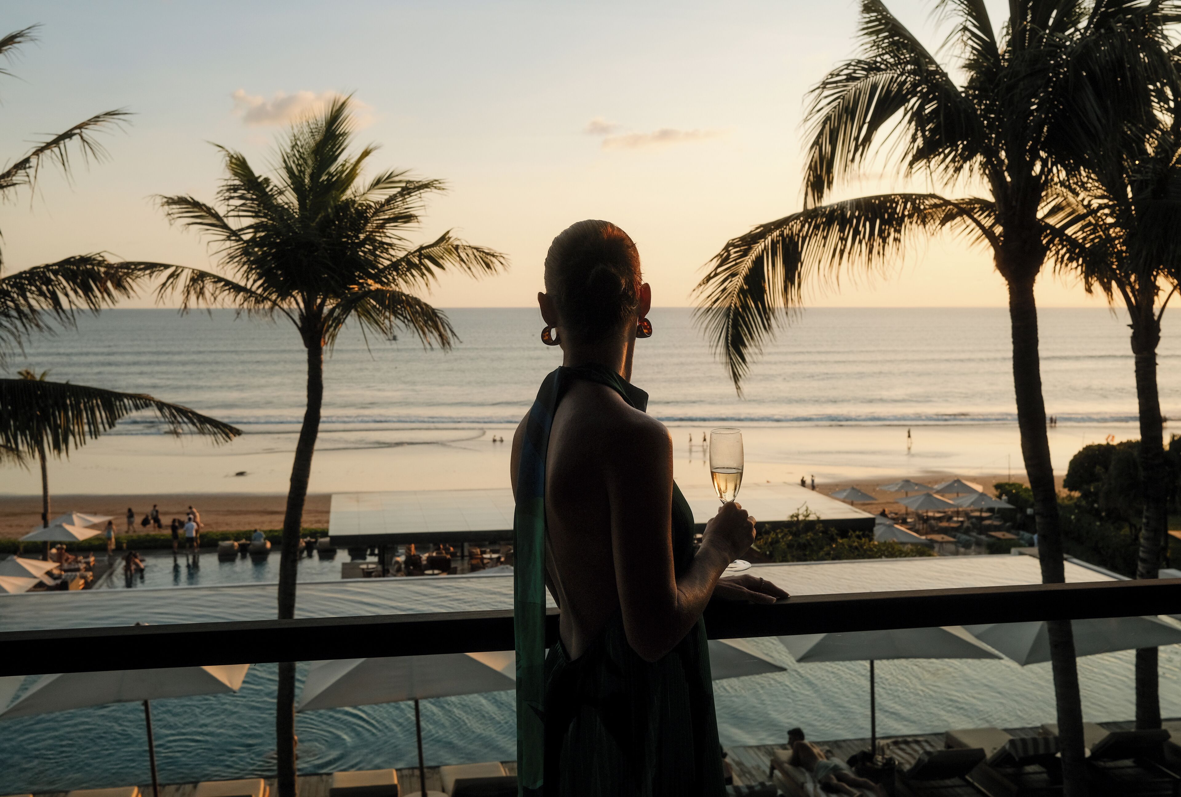 A person standing by a pool with a view of the ocean and palm trees.