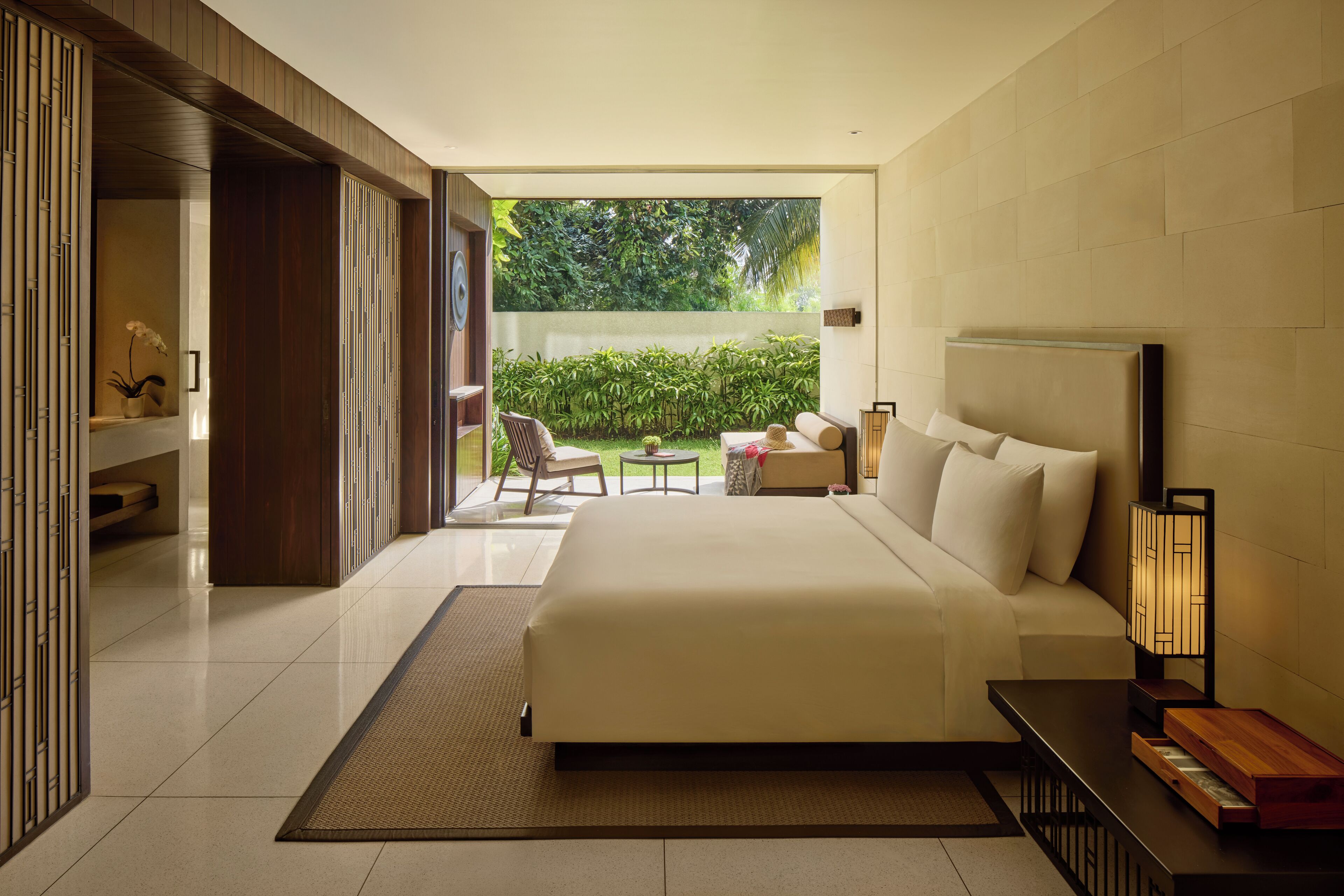 A modern hotel room with a large bed, a small table, and a view of a lush garden.
