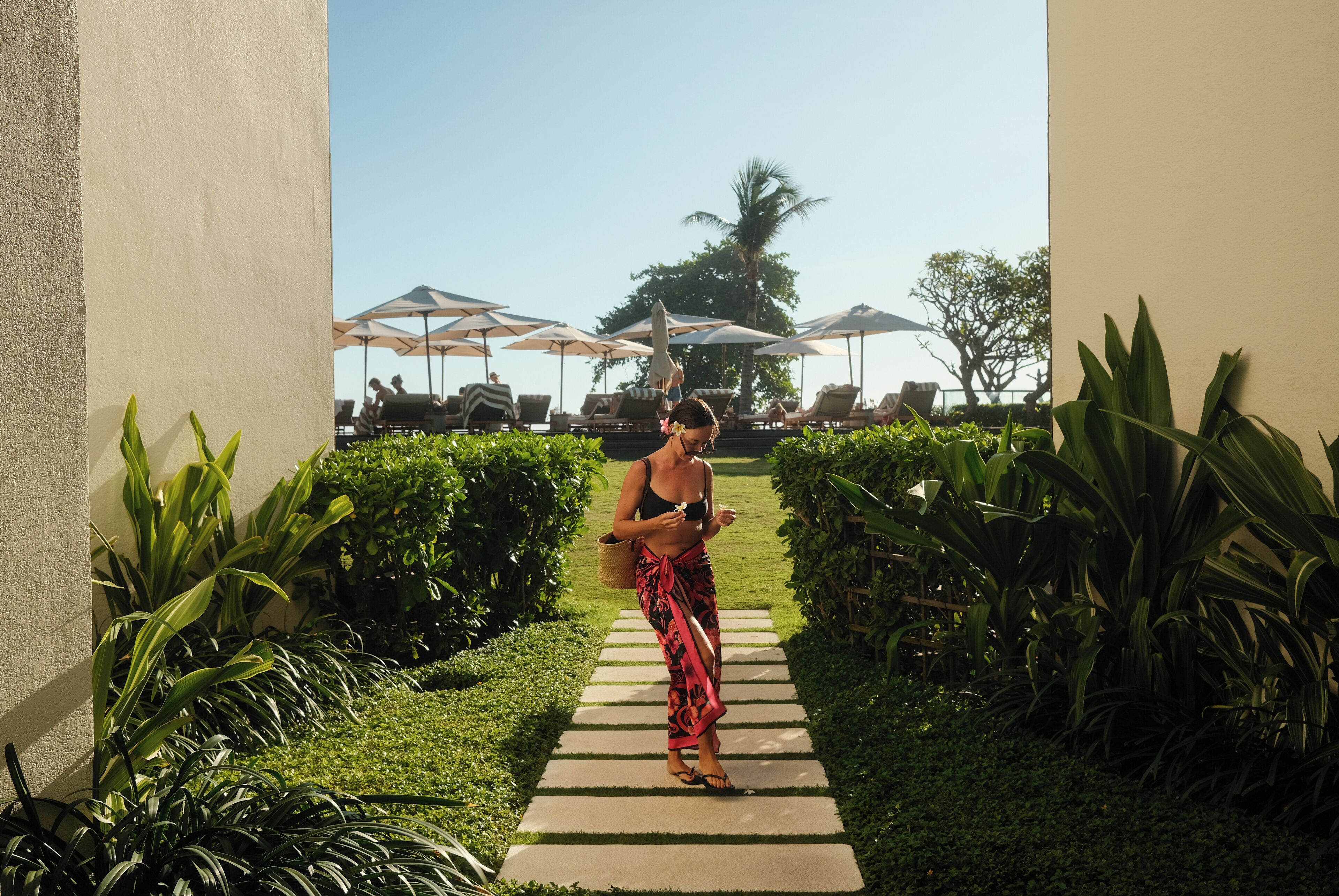 A pathway leading to a pool area with lounge chairs and umbrellas.
