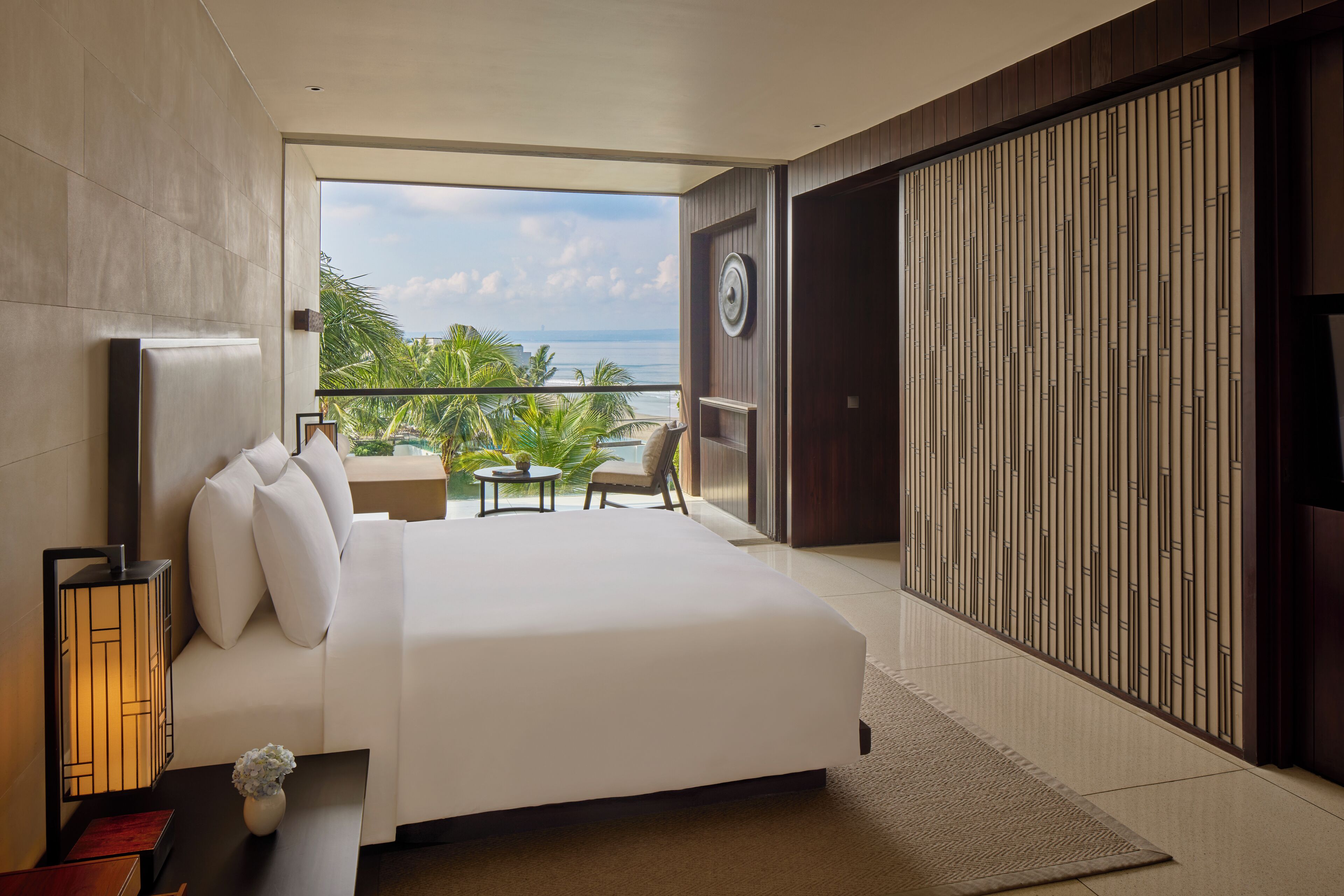 A modern hotel room with a large bed, a balcony with a view of the sea, and a traditional sliding door.