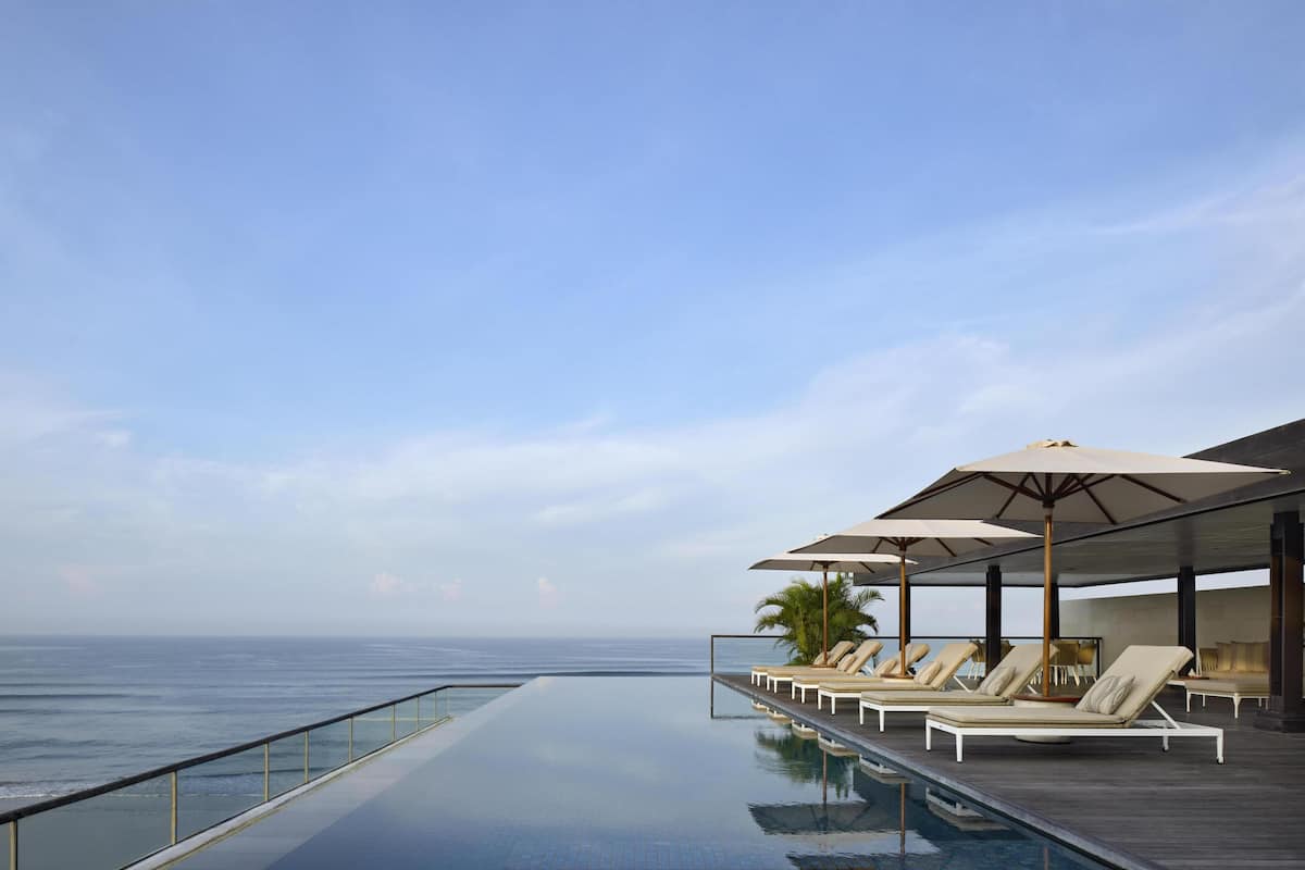 An infinity pool with a view of the ocean, lounge chairs, and umbrellas.