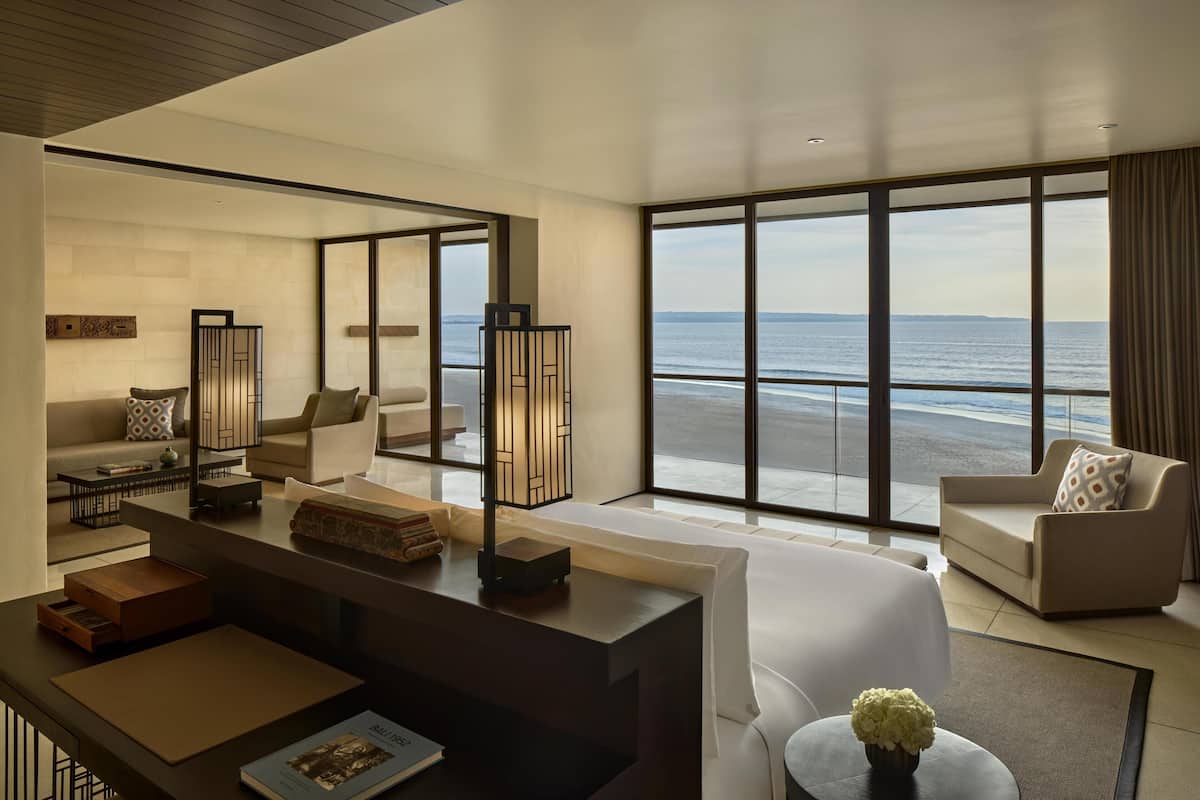 Una moderna camera d'hotel con un'ampia finestra vista mare, un'accogliente area salotto e una scrivania con una lampada.