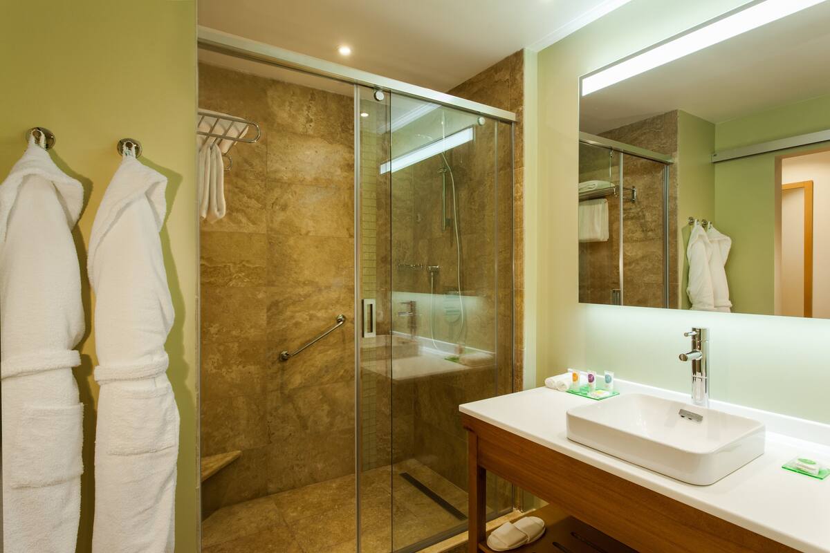 A modern bathroom with a glass-enclosed shower, a white sink, and two white towels hanging on hooks.