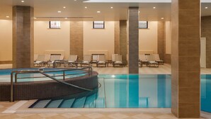 A modern indoor swimming pool with a tiled floor, lounge chairs, and a central staircase. - Grand Resort Jermuk (Jermuk)