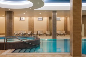 Une piscine intérieure moderne, dotée d’un sol carrelé, de chaises longues et d’un escalier central.
