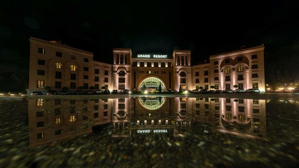 A grand resort building with a large arched entrance and a reflection in the water in front. - Grand Resort Jermuk (Jermuk)