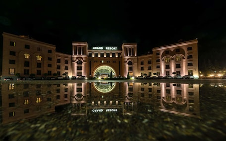 A grand resort building with a large arched entrance and a reflection in the water in front.