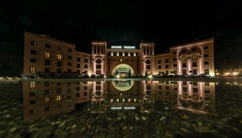 Un vaste bâtiment d’hôtel de luxe, doté d’une grande entrée en arc de cercle et dont l’image se reflète dans l’eau devant.