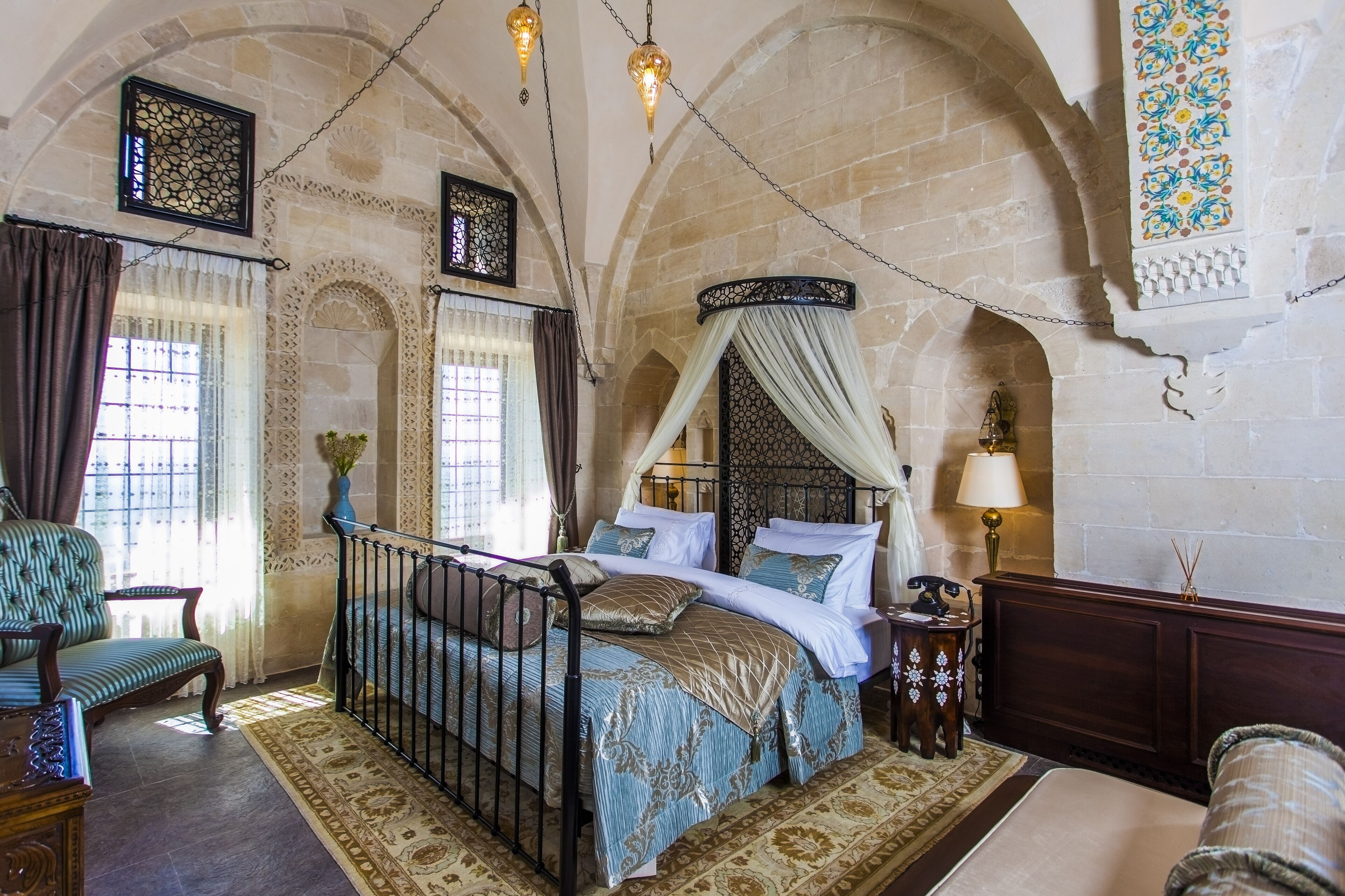 A bedroom with a four-poster bed, a nightstand, a chair, and a decorative wall.
