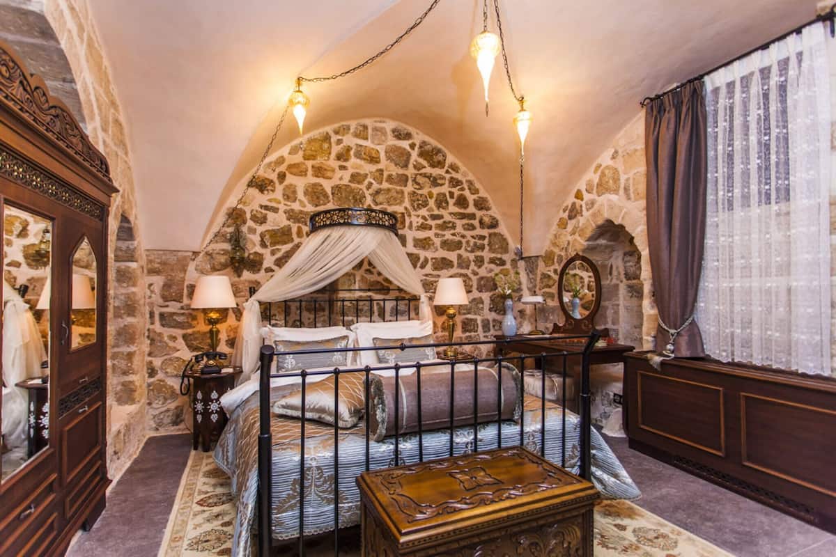 Quarto com paredes de pedra, cama de dossel, mesa de cabeceira, cômoda e espelho.