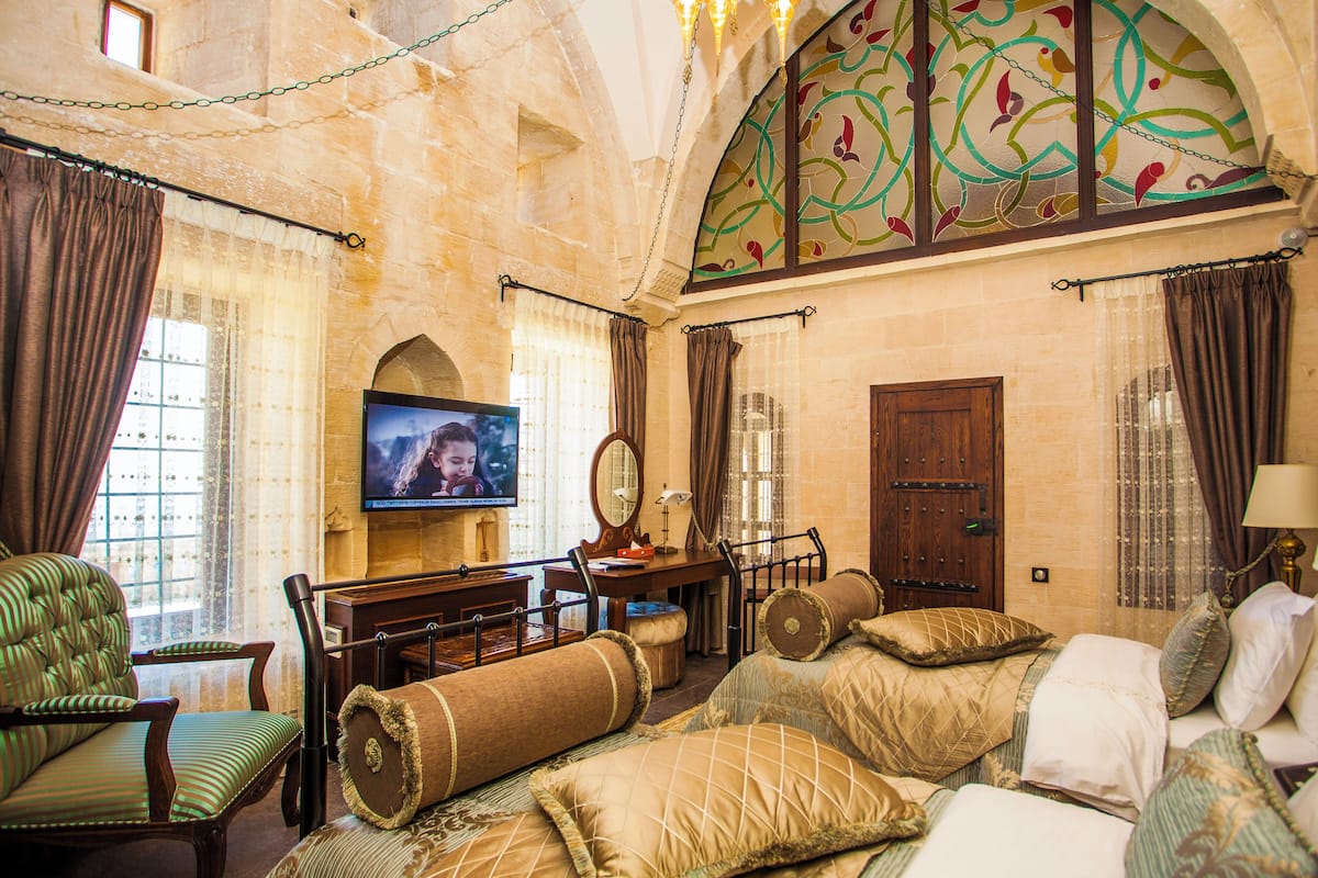 Quarto de hotel com uma cama grande, uma mesa de trabalho, televisão e vista para a cidade pela janela.