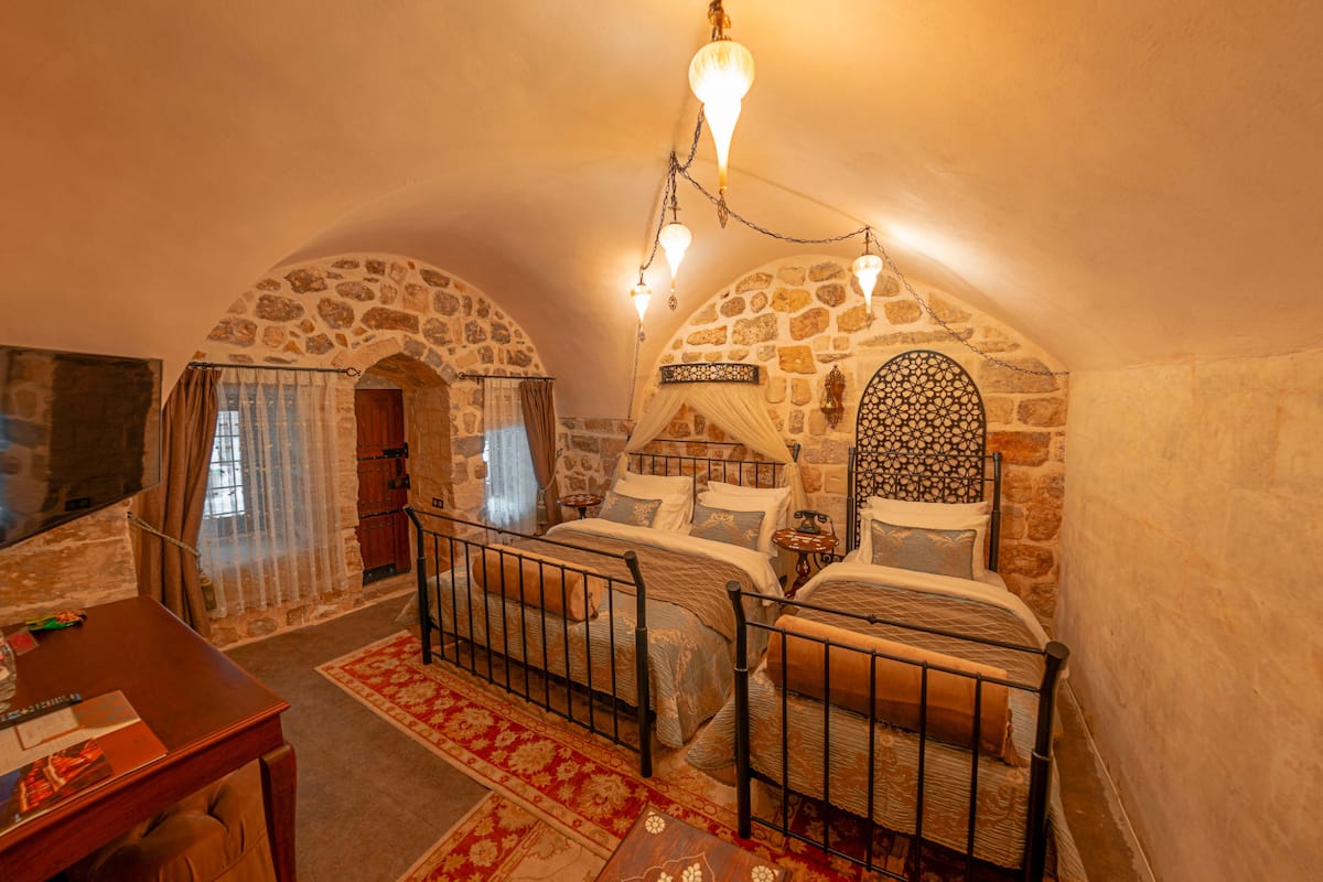 Um quarto aconchegante com um arco de pedra, uma cama com dossel e uma mesa com cadeira.