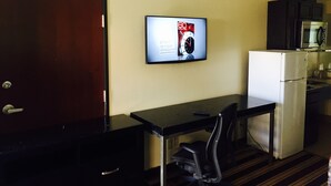 A compact hotel room with a kitchenette, a small dining table with a chair, and a TV mounted on the wall displaying a sports advertisement. - Executive Inn (Groves)