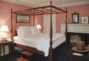A four-poster bed in a room with pink walls, a fireplace, and a framed picture above the bed. - Ships Inn (Nantucket)