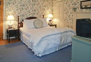 A neatly made bed with white linens, two bedside lamps, a wooden nightstand, and a television on a stand. - Ships Inn (Nantucket)