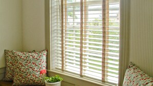 A room with a wooden bench against a window with blinds, two patterned pillows, and a potted plant. - Ships Inn (Nantucket)