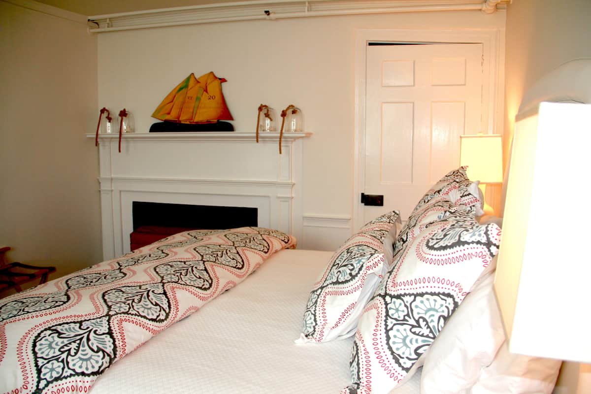 A bedroom with a bed, patterned bedding, a fireplace, and a door.