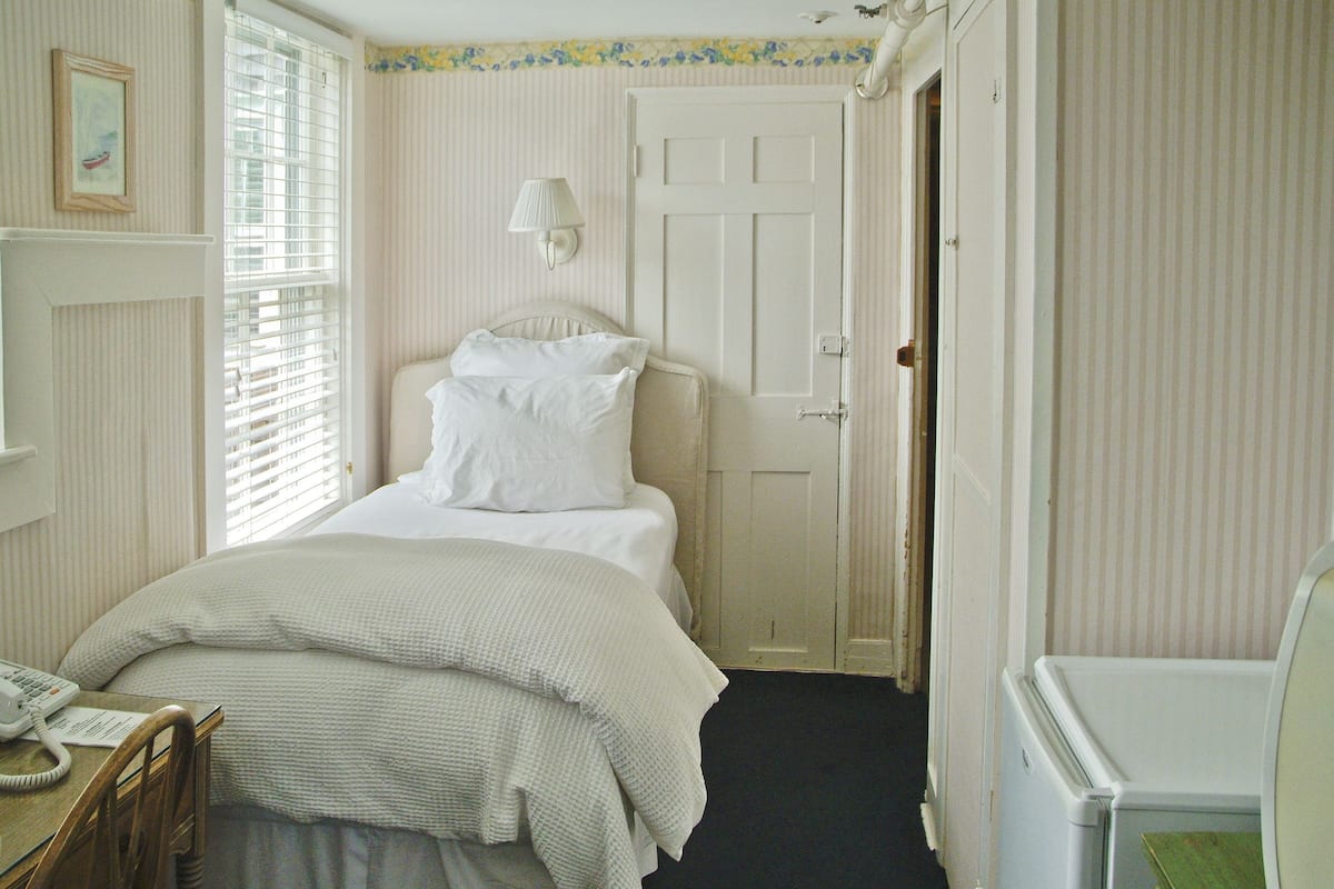 A bedroom with a bed, a bedside table with a lamp, a chair, and a desk with a telephone.