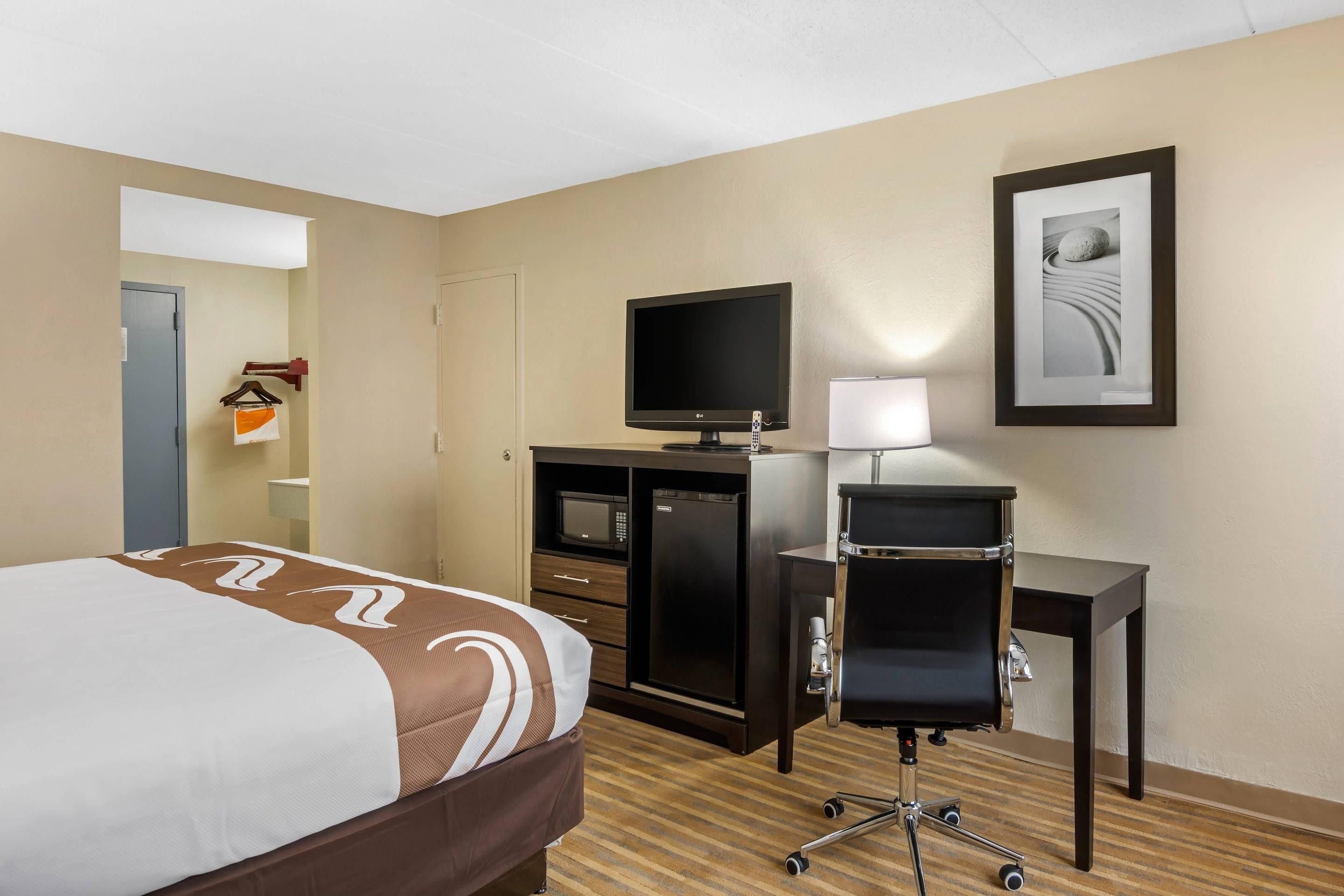 A hotel room with a bed, a desk with a computer, a television, and a framed picture on the wall.