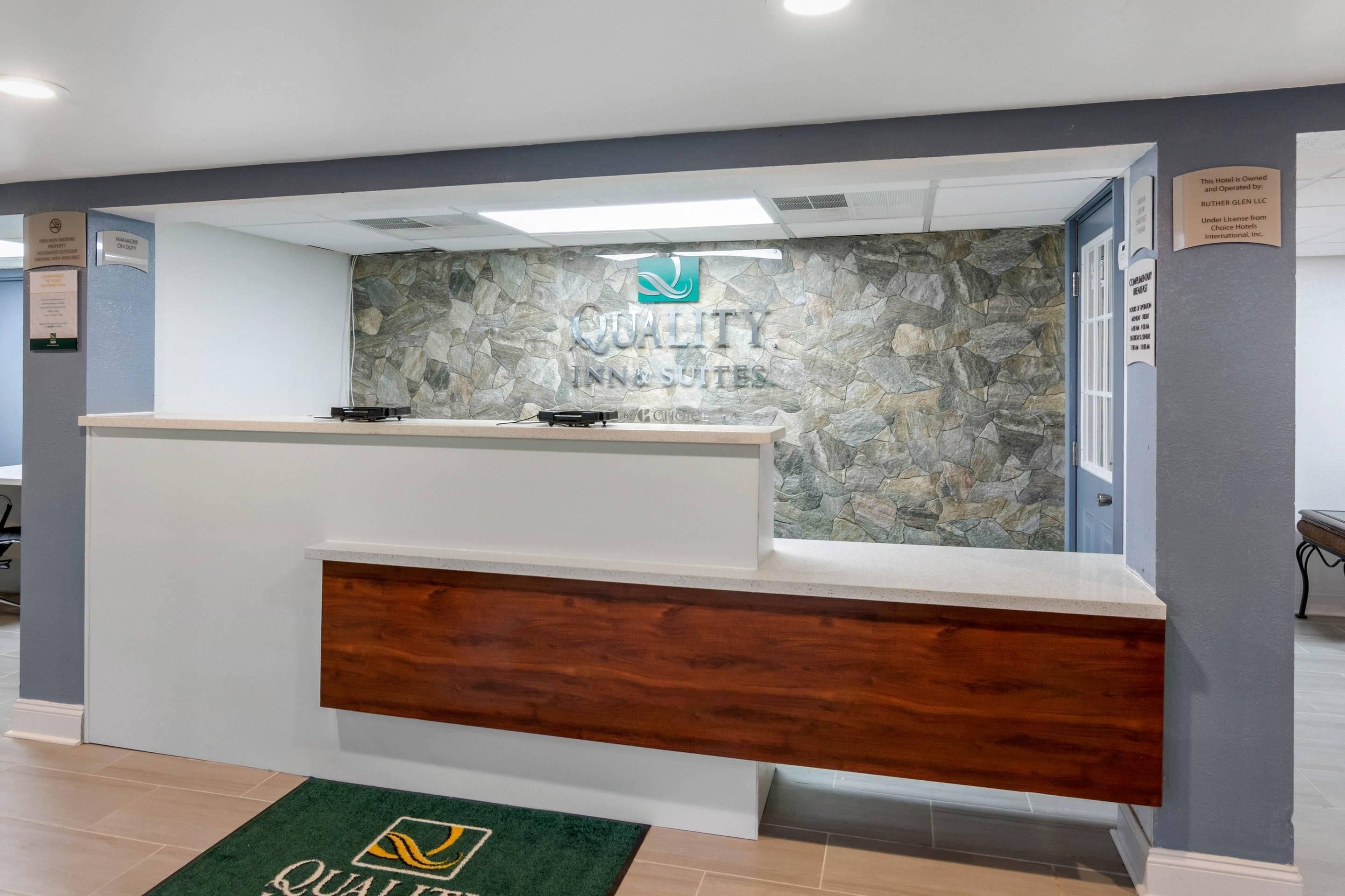 Un mostrador de recepción de hotel con un fondo de pared de piedra y una alfombra verde con el logotipo del hotel.