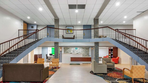 Un hall d’hôtel doté d’un comptoir d’accueil central, de deux escaliers et de plusieurs espaces aménagés pour s’asseoir.