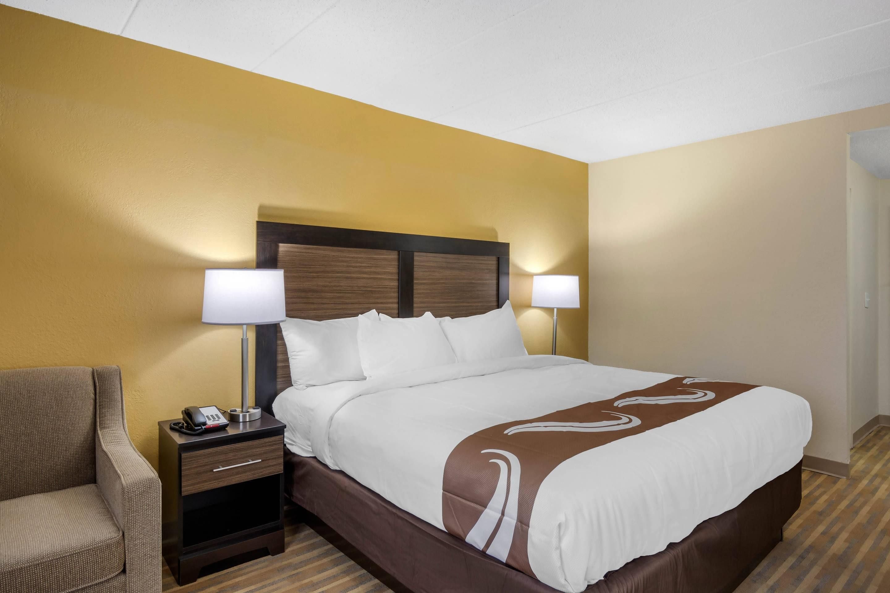 A hotel room with a bed, bedside lamps, a telephone, a chair, and a nightstand.
