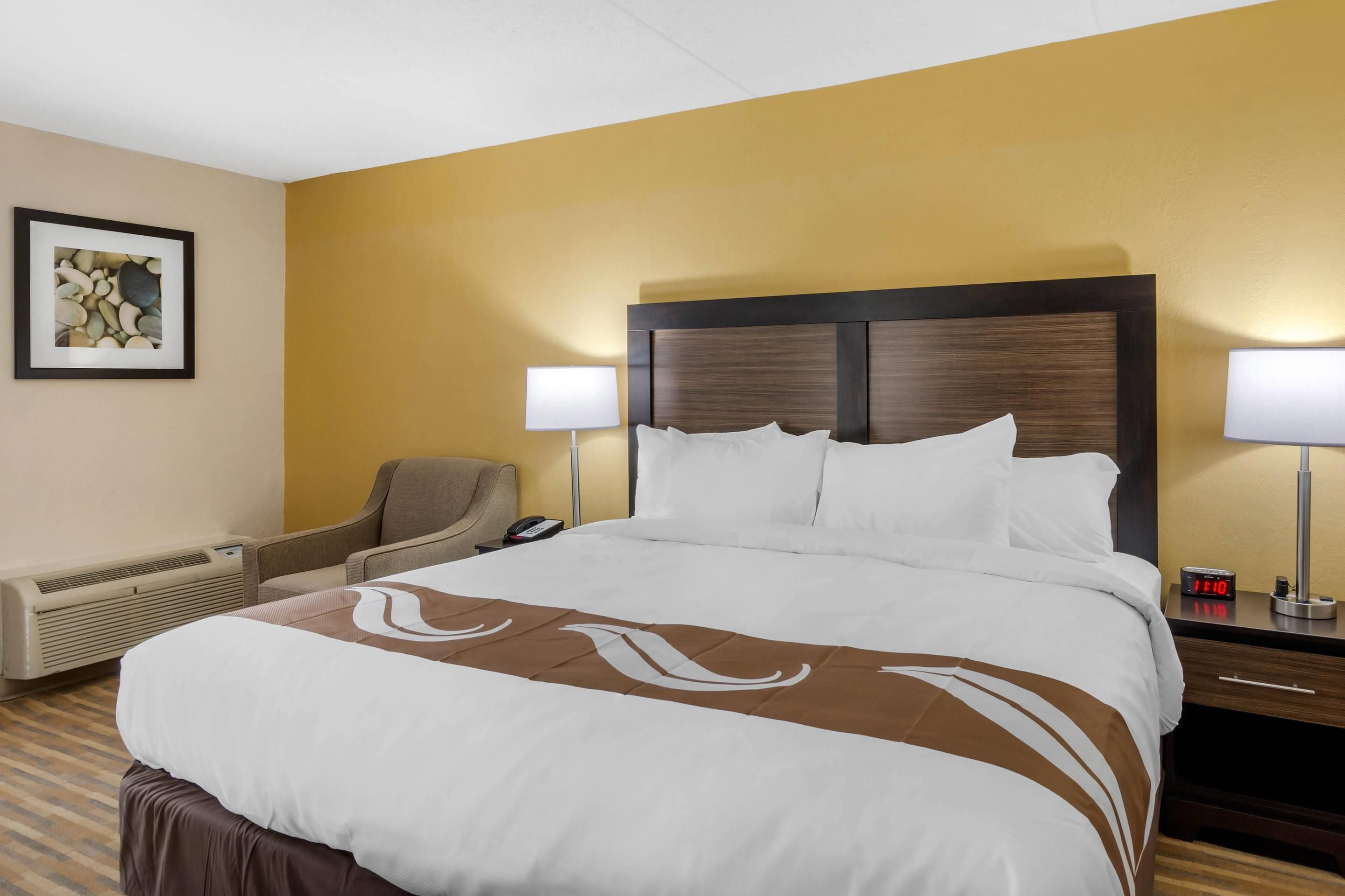 Habitación de hotel con una cama grande, dos lámparas de noche, una silla, un escritorio y un cuadro en la pared.