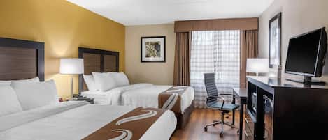 Habitación de hotel con dos camas, un escritorio, un televisor, una silla y una ventana con cortinas.