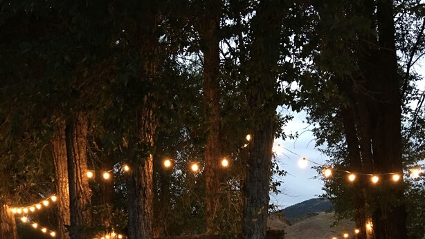 An outdoor seating area with string lights, wooden tables, chairs, and a hammock. - Black Bear Inn (Dubois)