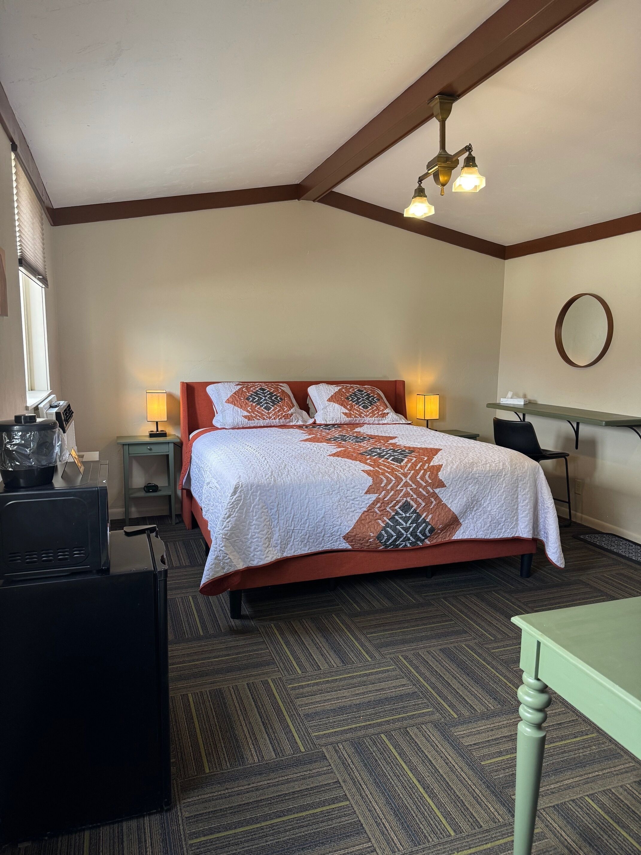 A hotel room with a bed, bedside lamps, a desk, a chair, and a window.