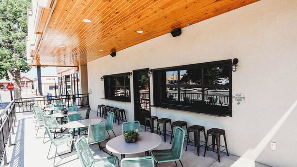 An outdoor seating area with round tables and chairs, a wooden ceiling, and large windows. - Hotel LaBonte (Douglas)