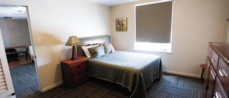 A bedroom with a bed, a nightstand, a lamp, a dresser, a ceiling fan, and a window.