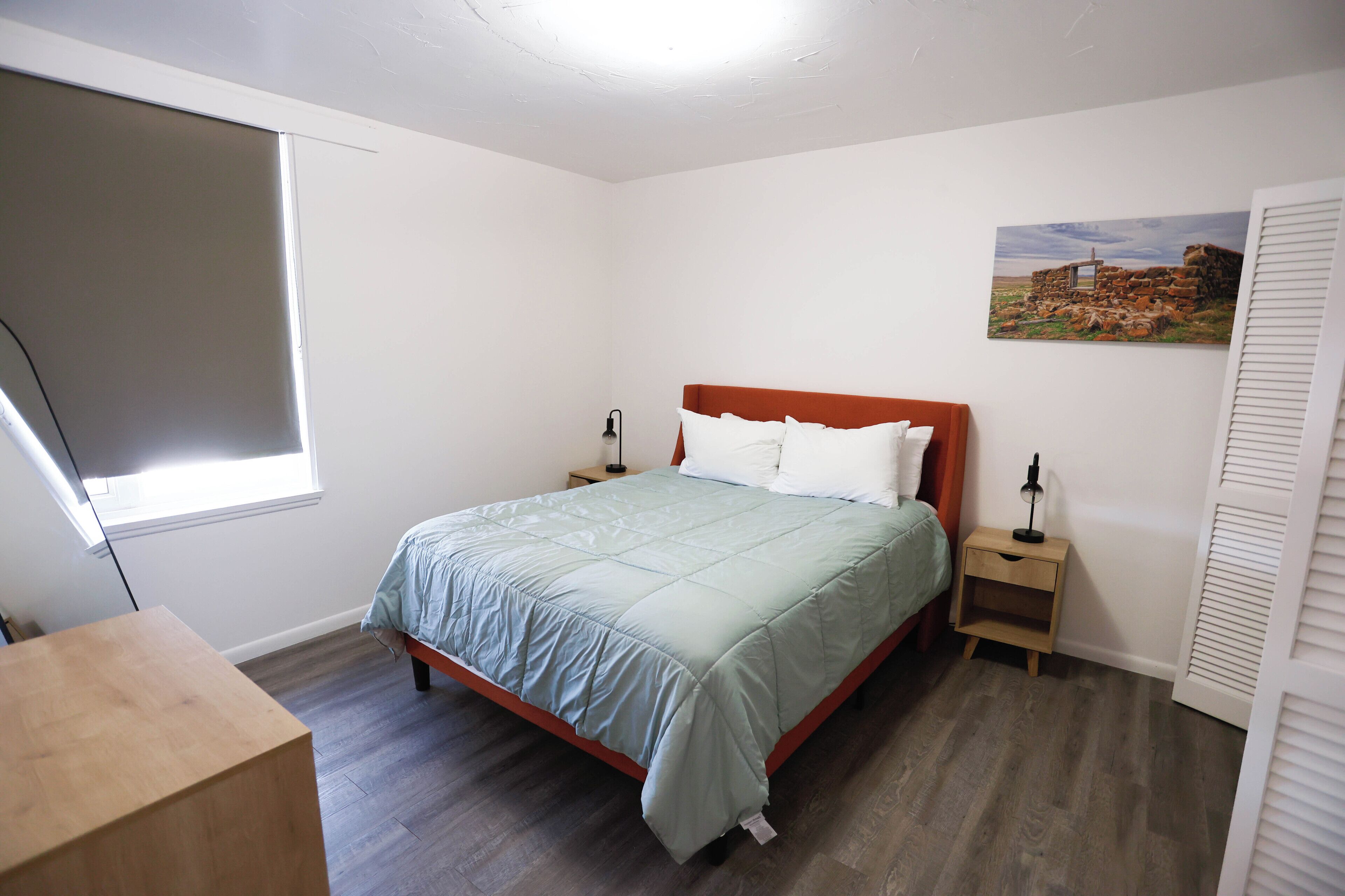 A bedroom with a bed, bedside tables, a window, and a painting on the wall.