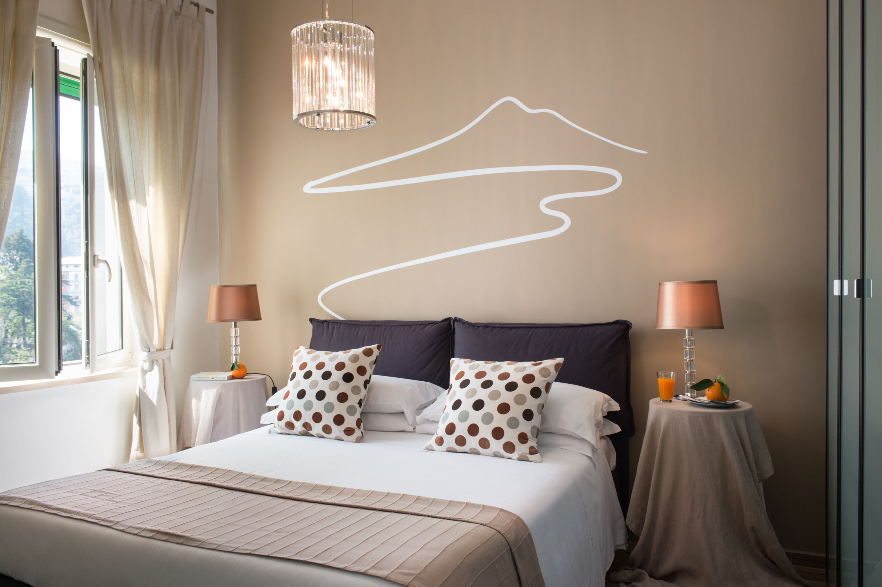A neatly arranged bedroom with a bed, two bedside tables with lamps, a wall art piece, and a window with curtains.