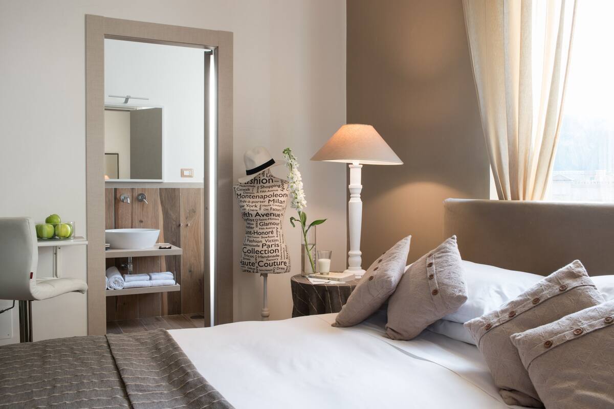 Une chambre d’hôtel comprenant un lit, une table de chevet avec une lampe, un miroir, une armoire et une salle de bain avec un lavabo et un porte-serviettes.